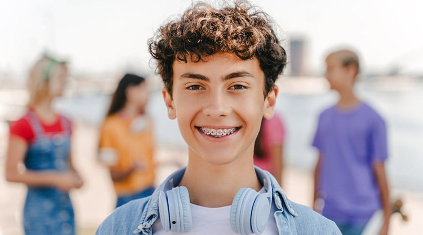 Smiling teen with braces and headphones around his neck outdoors with friends in the background at Delta Smiles in Antioch and Brentwood, CA